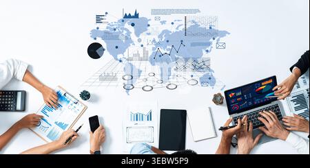 A diverse team collaborates on data analysis with laptops and documents on a map table, visualizing global trends and insights for strategic decision Stock Photo