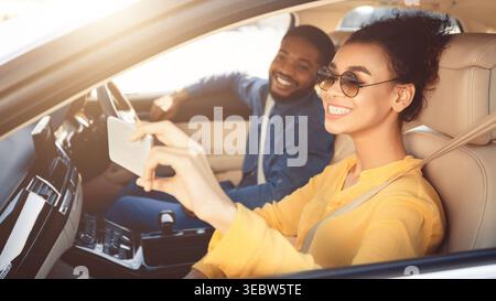 Couple Enjoying a Drive and Taking Selfies in a Modern Car During Sunny Weather Stock Photo