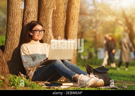 Young Woman Studying on Laptop in Park During Sunny Afternoon Stock Photo
