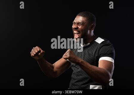 Mid-adult African man shouting, clenching fists and sweating in studio, black shirt with white trim Stock Photo
