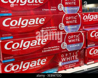 Rows of Colgate Optic White Advanced fluoride toothpaste boxes displayed on a retail shelf for dental hygiene product sales. Stock Photo