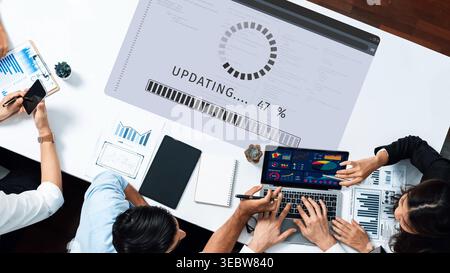 A collaborative workspace showcasing a laptop screen displaying update progress and colorful charts. Diverse individuals are focused on digital Stock Photo
