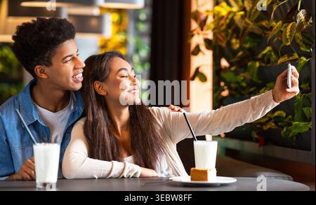 Young Couple Enjoys Sweet Moment Taking Selfie at Cozy Cafe With Drinks and Dessert Stock Photo