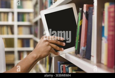 Afro student placing digital tablet on bookshelf Stock Photo