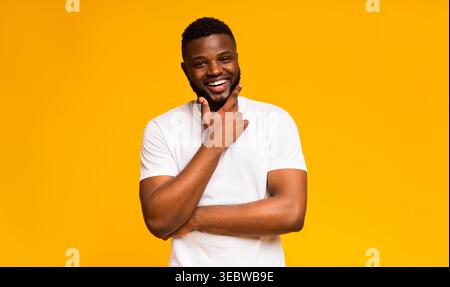 Man With Beard Smiles Joyfully Against a Bright Yellow Background While Posing Thoughtfully Stock Photo