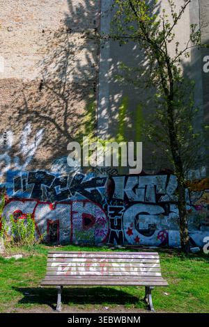 Empty park bench in front of a graffiti-covered wall in the Kreuzberg district of Berlin, Germany. Stock Photo