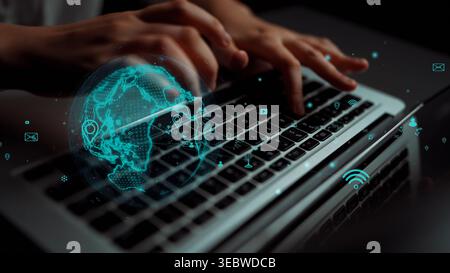 A person types on a laptop keyboard in a dark environment while a digital globe and connectivity symbols create a visionary landscape of technology Stock Photo