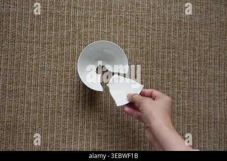 Hand holding piece of broken bowl on textured surface Stock Photo