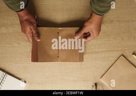 Hands hold a brown paper notebook on a wooden table Stock Photo