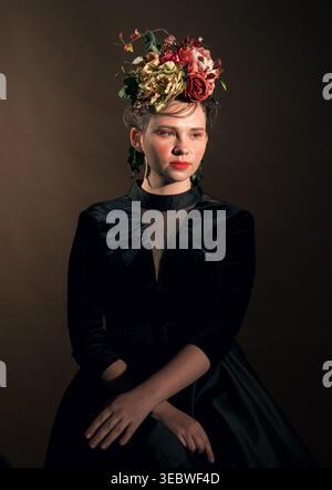Young woman in a black velvet dress and ornate floral headpiece poses elegantly in a studio Stock Photo