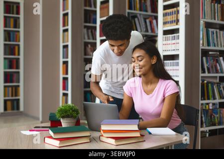 Students Collaborating Together in a Library While Using a Laptop and Studying Stock Photo