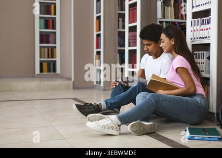 Students Studying Together in a Library While Using a Laptop and Reading Books Stock Photo
