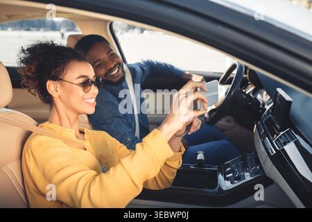 Happy Couple Taking Selfies Inside a Car During a Sunny Day in the City Stock Photo