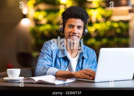 Young Man Studying With Laptop and Headphones in Modern Cafe Environment With Plants Stock Photo