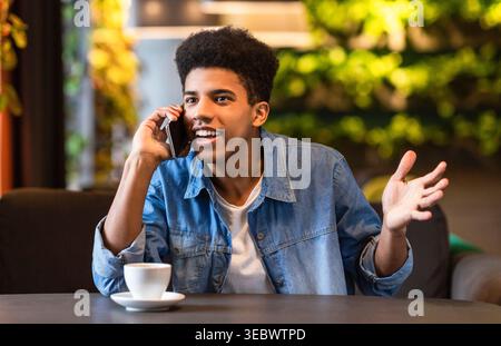 Young Man Engaged in a Lively Conversation While Enjoying Coffee in a Cozy Cafe Stock Photo