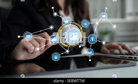 A businesswoman interacts with a digital display featuring various icons and graphs, representing data analytics and strategy development in a modern Stock Photo
