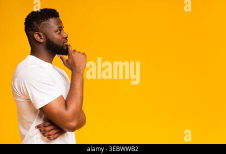 Man in White Shirt Thinking Against a Bright Yellow Background on a Sunny Day Stock Photo
