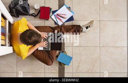 Student Working on Laptop Surrounded by Books and Stationery in a Study Area Stock Photo