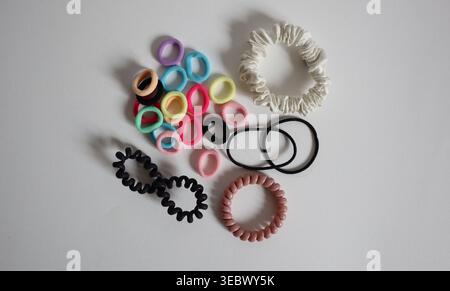 A collection of various hair ties and elastics is arranged on a white background. The ties include different colors and shapes, such as fabric, rubber, and plastic. Stock Photo