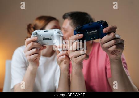 Portrait of loving couple enjoying home entertainment, holding wireless video game controllers, bonding over competitive or cooperative gameplay Stock Photo