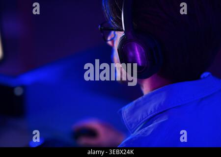 Young Man Engrossed in Gaming With Headphones in a Dimly Lit Room During Night Hours Stock Photo