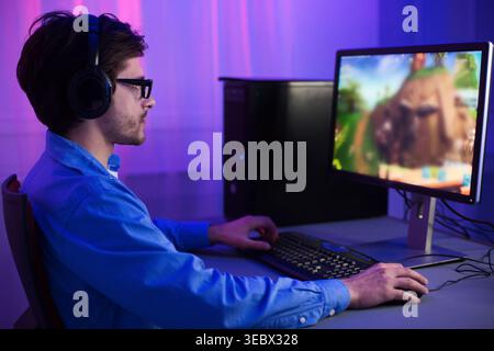 Young Man Engaging in Gaming at a Computer Setup in a Modern Room During Evening Hours Stock Photo