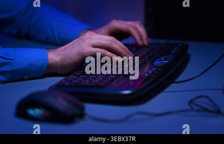 Hands Typing on a Keyboard in a Dimly Lit Room While Using a Computer Stock Photo