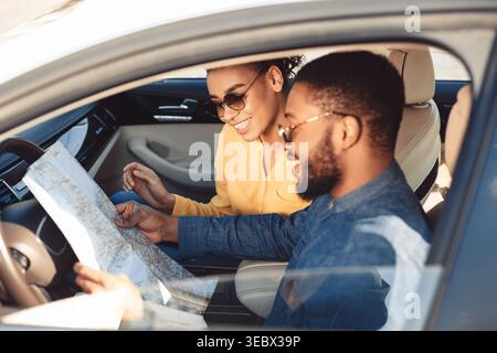 Young Couple Exploring a Map While Sitting in a Car During a Road Trip on a Sunny Day Stock Photo