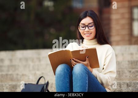 Young Woman Writing in Notebook While Sitting on Steps in Casual Outfit Stock Photo