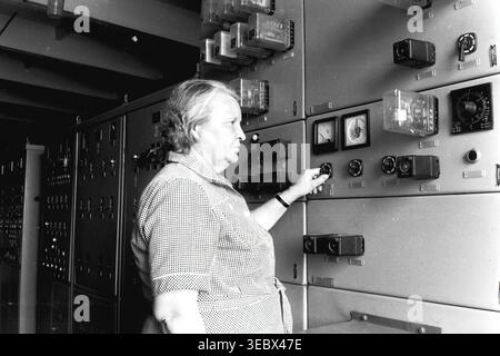 Slaviansk, 1986. At the traction power substation. An older female operator is adjusting switches on a large industrial electrical control panel covered with various analog meters, relays, and indicators. She is wearing a checkered short-sleeve shirt. The photograph captures the critical technical work required to maintain the city's trolleybus power supply during the Soviet era. This authentic archival image reflects the dedicated labor, complex infrastructure, and everyday industrial reality in the historical context of a peaceful Donbas. Stock Photo