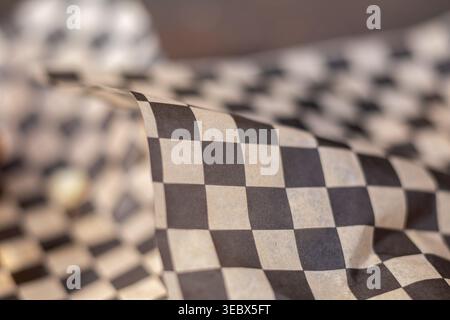 Black and white checkered paper covers food items. Paper wraps food, creating a checkered pattern. Folds and creases show soft, flexible texture. Grai Stock Photo