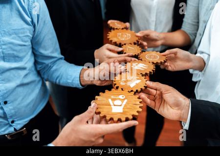 Hands of diverse professionals hold wooden cogs, each representing various facets of teamwork, strategy, and innovation in a collaborative business Stock Photo