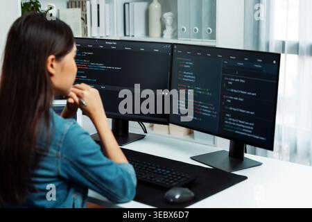 Young Asian IT developer looking online information on pc for beautiful pose with coding program data of website application, wearing jeans shirt Stock Photo