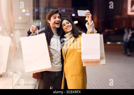 Couple Enjoys Shopping and Taking Selfies During Evening Outing in Vibrant City Stock Photo