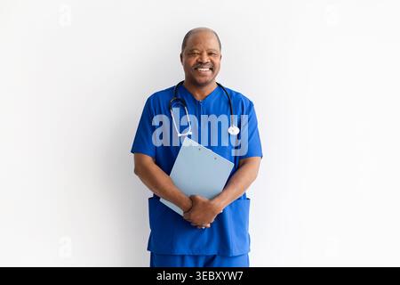 Cheerful mature African American male doctor in blue scrubs holding clipboard Stock Photo