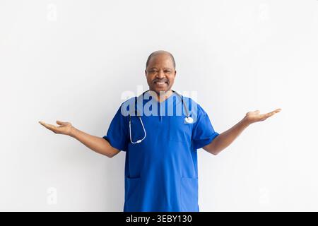 Friendly black male doctor in blue scrubs gesturing with both open hands Stock Photo