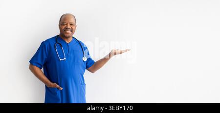 Smiling mature African American male doctor in blue scrubs gesturing open hand Stock Photo