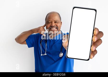 Smiling mature black male doctor in blue scrubs showing blank smartphone screen Stock Photo