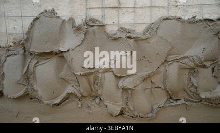 Plastering process on a wall using a metal mesh and cement mixture, creating a textured surface for building construction Stock Photo