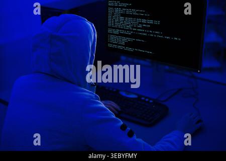 Person Working on Computer in Dimly Lit Room With Blue Lighting and Code on Screen Stock Photo