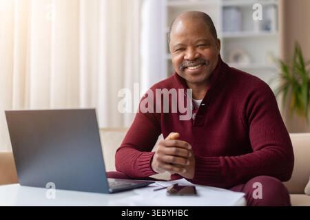 Confident smiling mature African American man sitting at laptop at home Stock Photo