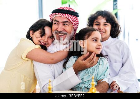 Arab grandfather smiling and embracing his happy grandchildren, showing family traditions, love, and multi-generational bonding in a warm middle easte Stock Photo