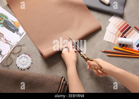 Female fashion designer cutting fabric on grey background Stock Photo