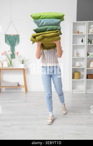 Woman holding stack of pillows with folded warm plaid in room Stock Photo