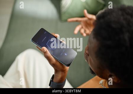 Black Man Using Smartphone Voice Assistant for Smart Home Control Stock Photo