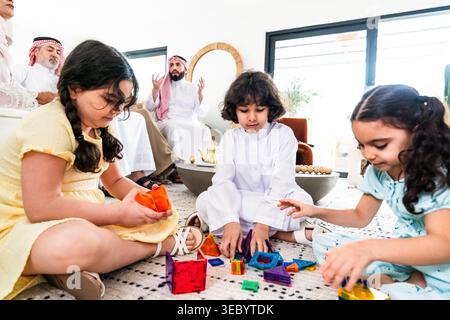 Arab family members spending quality time together at home, with children engaged in creative play on the rug and adults relaxing in the background, s Stock Photo