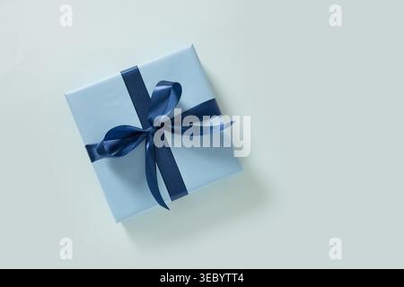 Blue gift box wrapped with ribbon bow on light background, minimal composition, holiday present concept, copy space, top view , clean modern style. Fa Stock Photo