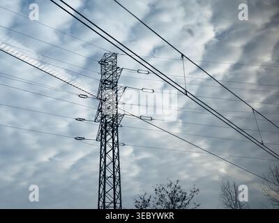 A powerful steel lattice pylon carries overhead power lines against a dramatic sky filled with textured clouds, representing energy distribution and i Stock Photo