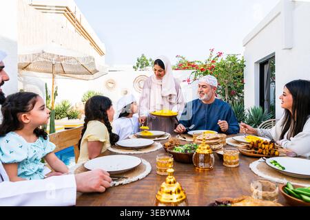 Middle eastern family gathering for an outdoor lunch or dinner, parents and children sitting around dining table in their house backyard, sharing food Stock Photo