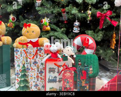 Plush gingerbread figures and stuffed toys, with candy cane and gift boxes, are displayed under a Christmas tree, evoking warmth and festive shopping Stock Photo